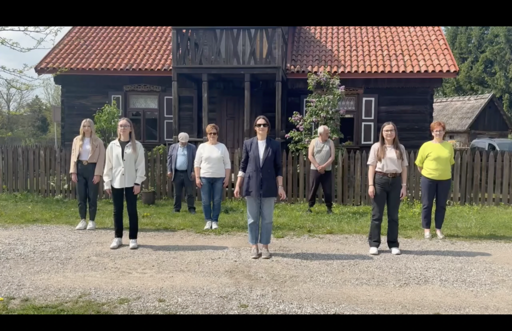 Uczestnicy akcji pomocy dla Olusia przed drewnianym budynkiem w Brańszczyku — kadr z filmu